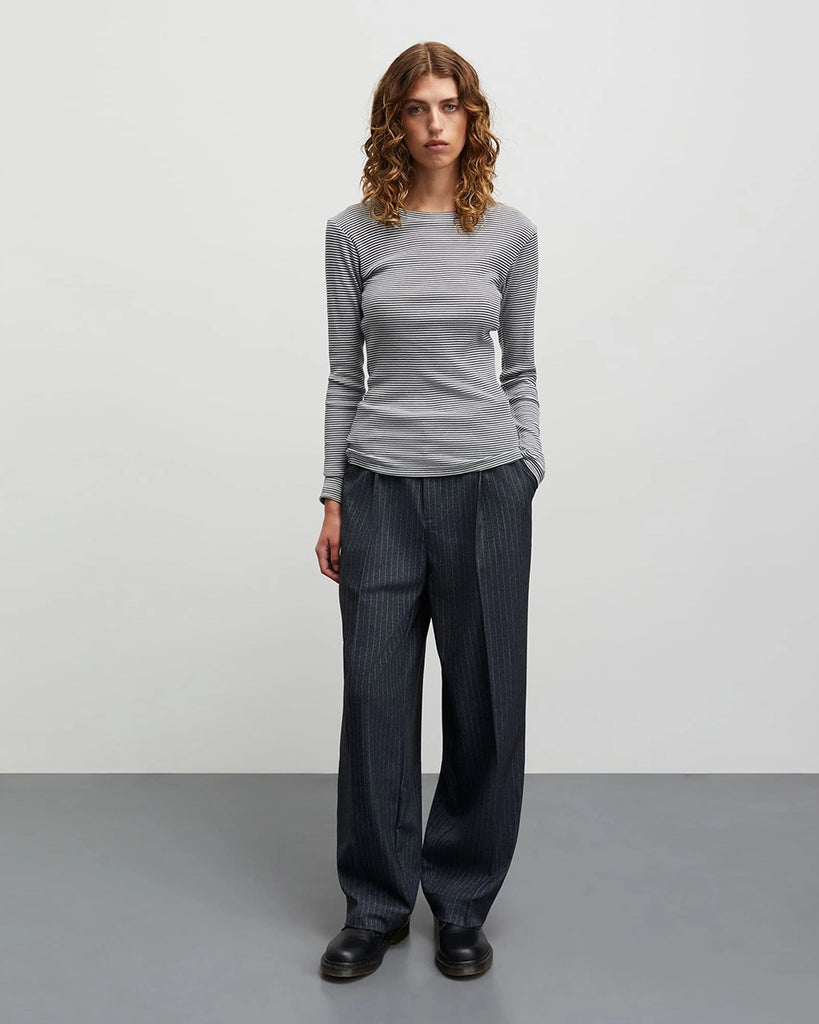 Minimalistyczny longsleeve 2x2 Tuba MADS NORGAARD w cienkie, granatowo-kremowe paski. Bluzka ma okrągły dekolt, przylegający fason i wąskie, długie rękawy. Wykonany jest z elastycznej, bawełnianej tkaniny z prążkowaną fakturą