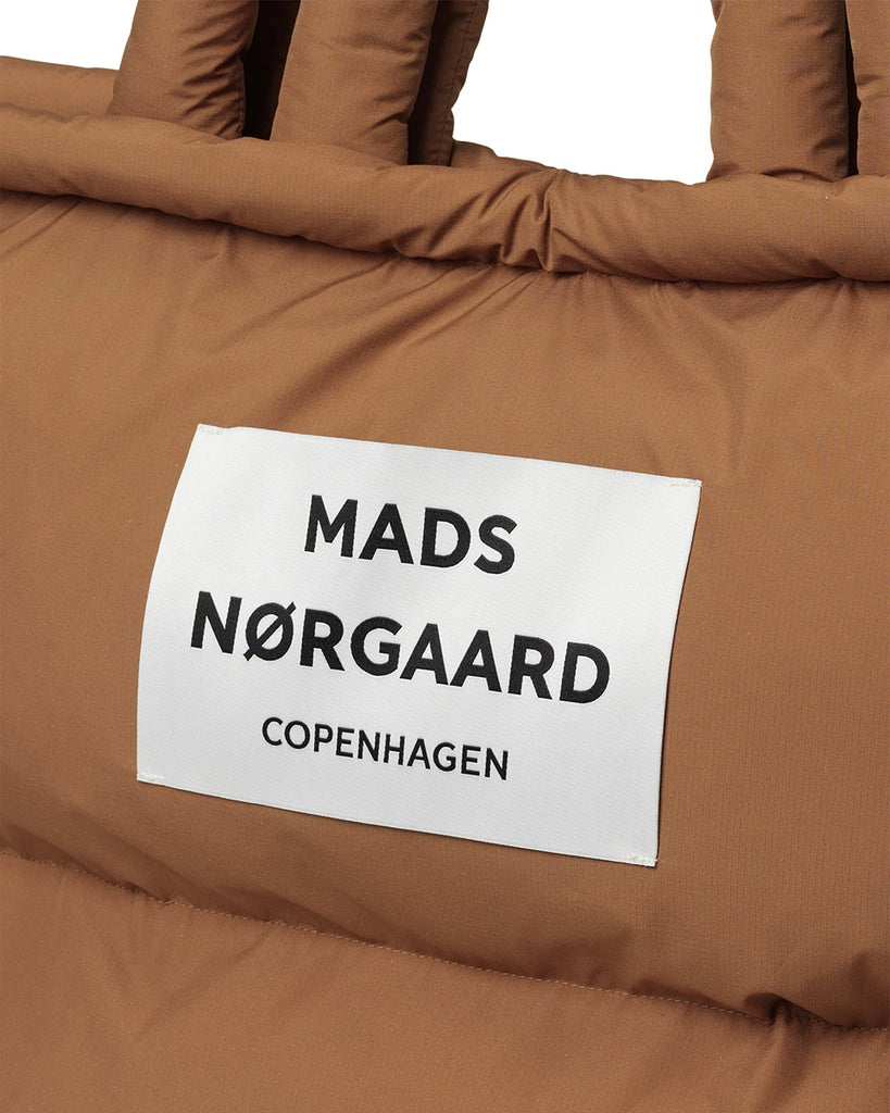 Duża, puchowa torba Pillow duńskiej marki MADS NØRGAARD w stylu shopper. Posiada dwie, krótkie rączki do wygodnego trzymania w dłoni i dwie dłuższe do zawieszenia na ramieniu