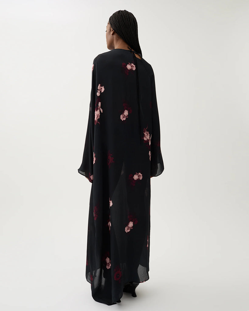 Długa, luźna sukienka Marge Wine Black w kolorze czarnym z kwiatowym printem. Ma okrągły dekolt z wiązaniem z tyłu oraz raglanowe, przedłużone rękawy. Dół sukienki jest asymetryczny.&nbsp;