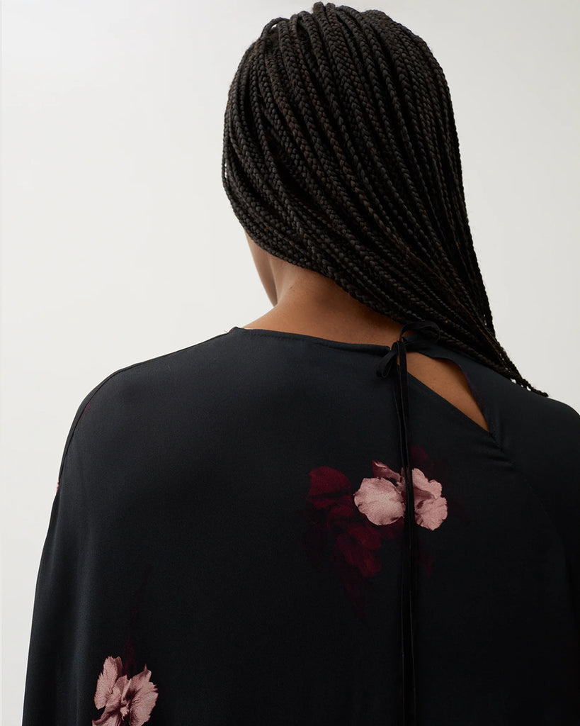 Długa, luźna sukienka Marge Wine Black w kolorze czarnym z kwiatowym printem. Ma okrągły dekolt z wiązaniem z tyłu oraz raglanowe, przedłużone rękawy. Dół sukienki jest asymetryczny.&nbsp;