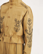 Krótka, strukturalna kurtka Maria Beige Antik Batik o nowoczesnym, nieco geometrycznym kroju. Posiada charakterystyczną, bardzo wysoką stójkę zapinaną na guziki. Regulowana w pasie za pomocą ściągacza ze sznurkami, co tworzy efekt delikatnej baskinki/falbany. Z przodu na kieszeniach oraz na rękawach znajdują się hafty z motywami roślinnymi i kwiatowymi. Dodatkowe, drobne, haftowane przeszycia ozdabiają również linię ramion. Zapinana na guziki.&nbsp;

-Krótki, nowoczesny fason

-Hafty z motywami roślinnymi i