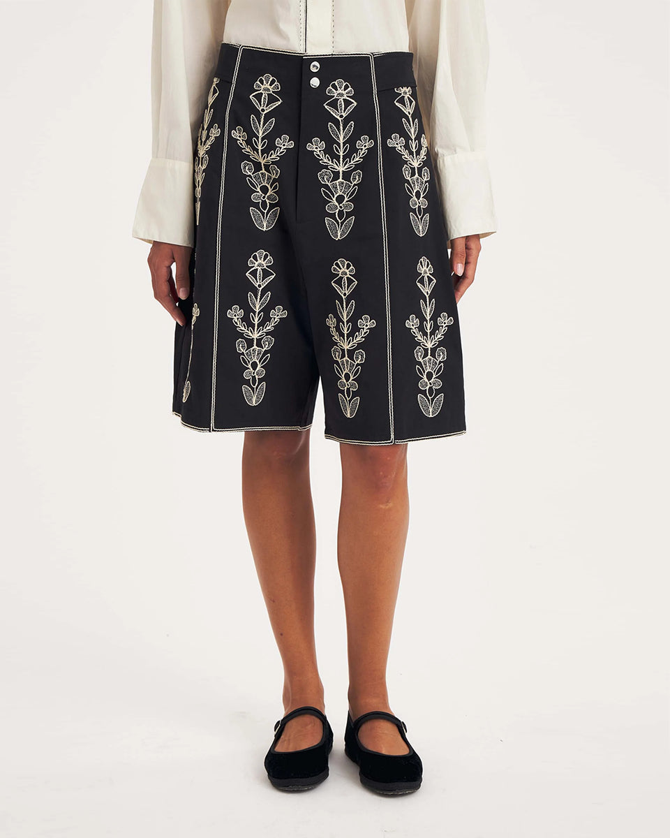 Dłuższe, eleganckie szorty typu bermudy Maria Black marki Antik Batik sięgające do kolan. Mają luźne, szerokie i prosto ścięte nogawki oraz wysoki stan z szerokim pasem i szlufkami. Zapinane są z przodu na dwa jasne guziki umieszczone pionowo. Wzdłuż nogawek oraz wokół kieszeni i paska mają kontrastowe, jasne lamówki. Przód, jak i tył zdobią bogate białe hafty o motywie roślinnym. Hafty umieszczone są symetrycznie w pionowych rzędach, co nawiązuje do tradycyjnego stylu boho.&nbsp;

-Luźne, proste nogawki

-