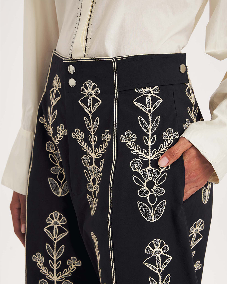 Dłuższe, eleganckie szorty typu bermudy Maria Black marki Antik Batik sięgające do kolan. Mają luźne, szerokie i prosto ścięte nogawki oraz wysoki stan z szerokim pasem i szlufkami. Zapinane są z przodu na dwa jasne guziki umieszczone pionowo. Wzdłuż nogawek oraz wokół kieszeni i paska mają kontrastowe, jasne lamówki. Przód, jak i tył zdobią bogate białe hafty o motywie roślinnym. Hafty umieszczone są symetrycznie w pionowych rzędach, co nawiązuje do tradycyjnego stylu boho.&nbsp;

-Luźne, proste nogawki

-