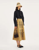 Rozkloszowana, trapezowa spódnica Maria Beige marki Antik Batik o klasycznej długości midi, sięgającej do połowy łydki. Ma wysoką, gładką talię z wyraźnie zaznaczonym, szerokim pasem. Głównym elementem dekoracyjnym są duże, pionowe hafty roślinne i kwiatowe w ciemnym kolorze. Haft układa się symetrycznie, w pionowe rzędy, co optycznie wydłuża sylwetkę i nadaje całości tradycyjny, rzemieślniczy charakter.&nbsp;

-Długość midi

-Wysoki stan

-Ozdobne hafty kwiatowe i roślinne

-Zamów spódnicę w swoim standard