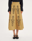Rozkloszowana, trapezowa spódnica Maria Beige marki Antik Batik o klasycznej długości midi, sięgającej do połowy łydki. Ma wysoką, gładką talię z wyraźnie zaznaczonym, szerokim pasem. Głównym elementem dekoracyjnym są duże, pionowe hafty roślinne i kwiatowe w ciemnym kolorze. Haft układa się symetrycznie, w pionowe rzędy, co optycznie wydłuża sylwetkę i nadaje całości tradycyjny, rzemieślniczy charakter.&nbsp;

-Długość midi

-Wysoki stan

-Ozdobne hafty kwiatowe i roślinne

-Zamów spódnicę w swoim standard