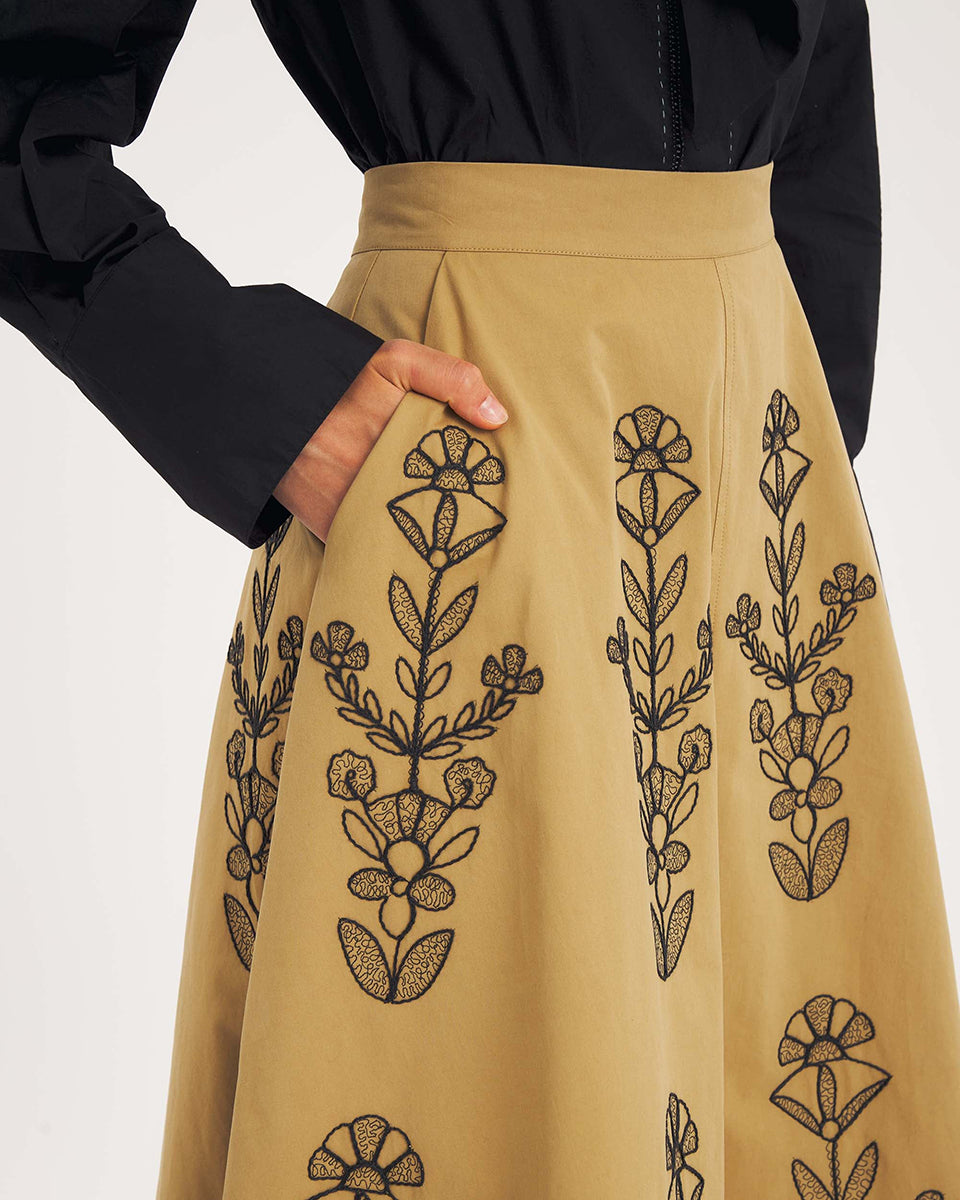 Rozkloszowana, trapezowa spódnica Maria Beige marki Antik Batik o klasycznej długości midi, sięgającej do połowy łydki. Ma wysoką, gładką talię z wyraźnie zaznaczonym, szerokim pasem. Głównym elementem dekoracyjnym są duże, pionowe hafty roślinne i kwiatowe w ciemnym kolorze. Haft układa się symetrycznie, w pionowe rzędy, co optycznie wydłuża sylwetkę i nadaje całości tradycyjny, rzemieślniczy charakter.&nbsp;

-Długość midi

-Wysoki stan

-Ozdobne hafty kwiatowe i roślinne

-Zamów spódnicę w swoim standard