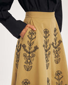 Rozkloszowana, trapezowa spódnica Maria Beige marki Antik Batik o klasycznej długości midi, sięgającej do połowy łydki. Ma wysoką, gładką talię z wyraźnie zaznaczonym, szerokim pasem. Głównym elementem dekoracyjnym są duże, pionowe hafty roślinne i kwiatowe w ciemnym kolorze. Haft układa się symetrycznie, w pionowe rzędy, co optycznie wydłuża sylwetkę i nadaje całości tradycyjny, rzemieślniczy charakter.&nbsp;

-Długość midi

-Wysoki stan

-Ozdobne hafty kwiatowe i roślinne

-Zamów spódnicę w swoim standard