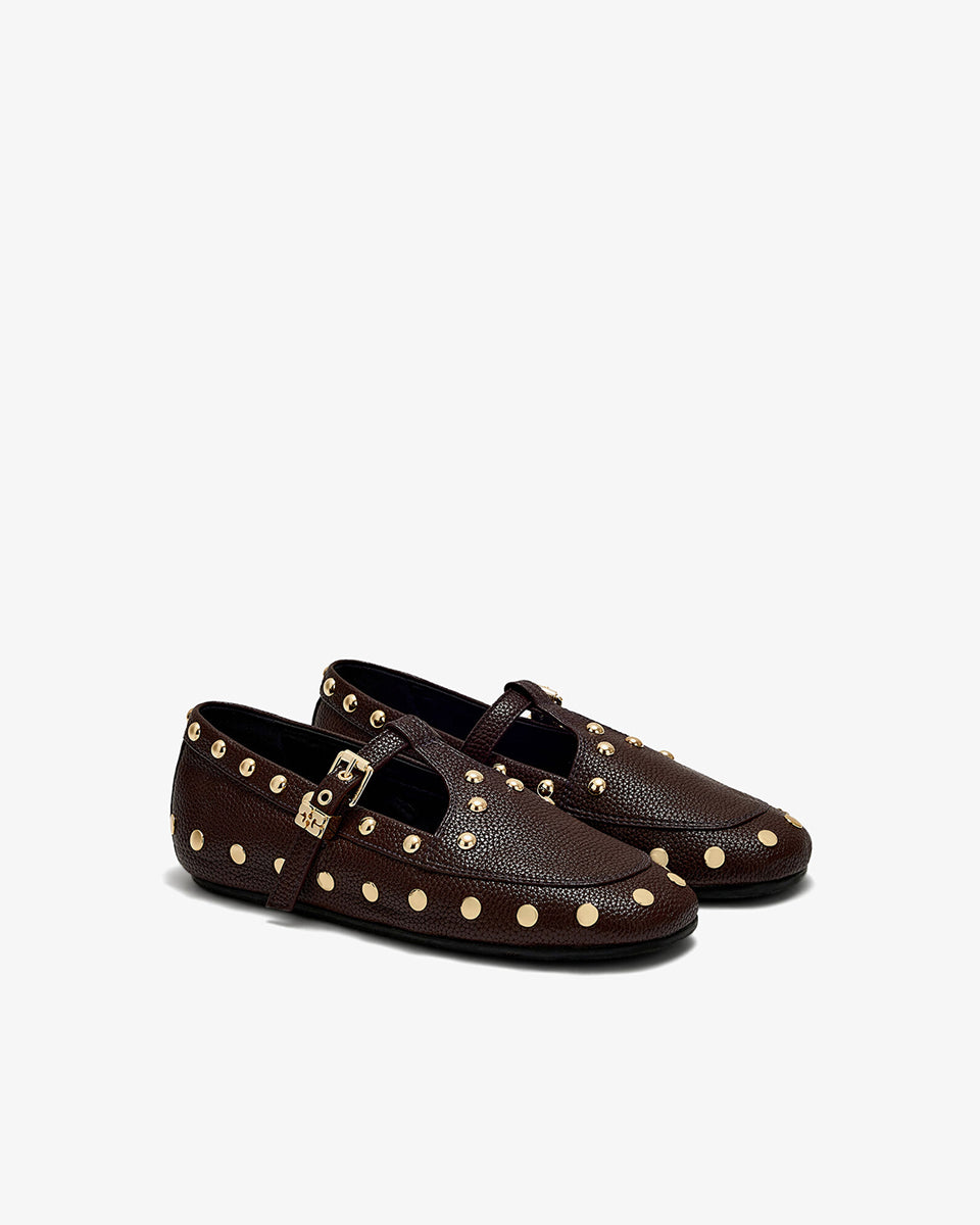 Płaskie, ciemnobrązowe mokasyny Mary Jenny Studs GANNI Chicory Coffee o zaokrąglonych noskach. Cholewkę zdobią liczne, gęsto rozmieszczone złote piny (ćwieki). Posiadają regulowane paski zapinane na złotą klamrę zakończoną charakterystycznym logo GANNI Butterfly po zewnętrznej stronie stopy. Buty mają wyraźną, groszkowaną fakturę. Rozmiarówka jest standardowa, a wysokość obcasa to 0,7 cm.

-Standardowa rozmiarówka