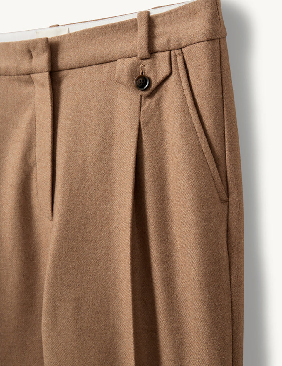Proste, eleganckie spodnie Mitch Camel o klasycznym, lekko luźnym kroju z długimi nogawkami. Mają średni stan z dopasowanym pasem i zaszewkami z przodu, co podkreśla sylwetkę i dodaje formalnego charakteru. Z tyłu znajdują się kieszenie z lamówkami, a jedna z nich zapinana jest na guzik. Wykonane z tkaniny z wełną z recyklingu.