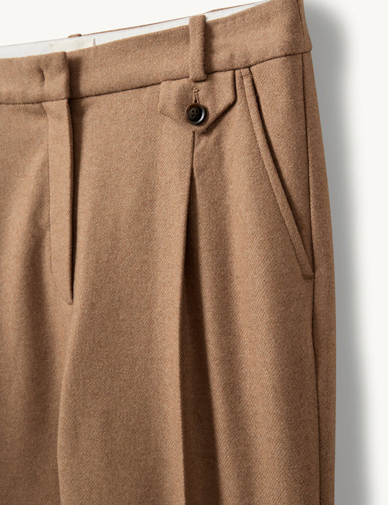 Proste, eleganckie spodnie Mitch Camel o klasycznym, lekko luźnym kroju z długimi nogawkami. Mają średni stan z dopasowanym pasem i zaszewkami z przodu, co podkreśla sylwetkę i dodaje formalnego charakteru. Z tyłu znajdują się kieszenie z lamówkami, a jedna z nich zapinana jest na guzik. Wykonane z tkaniny z wełną z recyklingu.