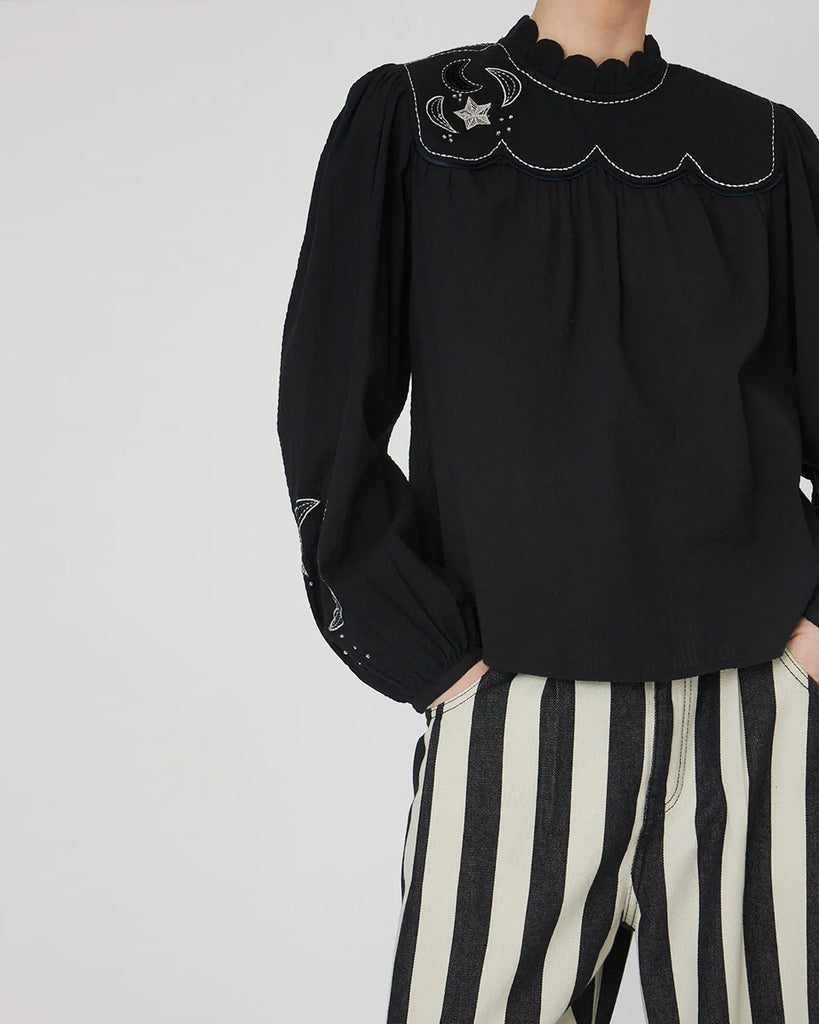 Bawełniana bluzka Embroidered Moon&amp;Star marki STELLA NOVA z muszelkowym kołnierzykiem pod szyję i długimi rękawami. Zdobiona haftowanymi motywami gwiazd i księżyca. Rękawy wykończone są mankietami z rozcięciem zapinanym na guzik oraz marszczeniami u góry, które nadają im bufiastego charakteru. Z tyłu znajduje się rozcięcie z guzikiem i pętelką do zapięcia.&nbsp;