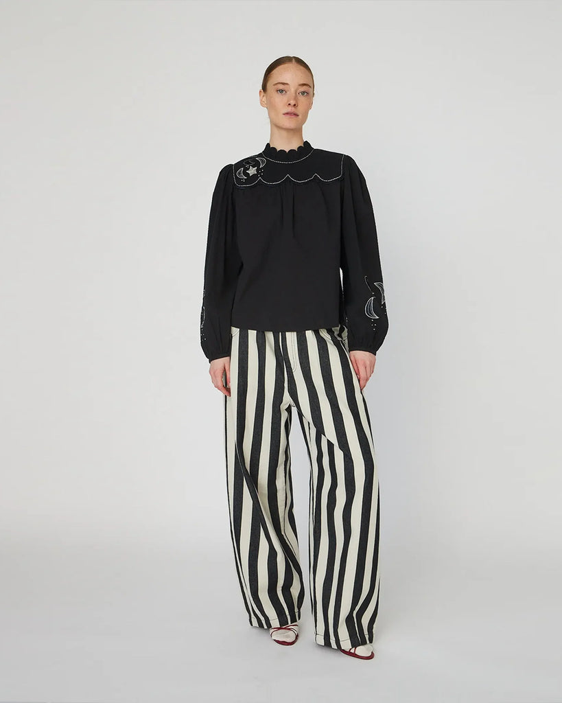 Bawełniana bluzka Embroidered Moon&amp;Star marki STELLA NOVA z muszelkowym kołnierzykiem pod szyję i długimi rękawami. Zdobiona haftowanymi motywami gwiazd i księżyca. Rękawy wykończone są mankietami z rozcięciem zapinanym na guzik oraz marszczeniami u góry, które nadają im bufiastego charakteru. Z tyłu znajduje się rozcięcie z guzikiem i pętelką do zapięcia.&nbsp;