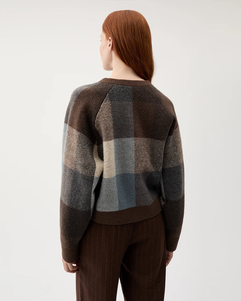 Pudełkowy, ciepły sweter Nina Chicory Coffee w wielokolorową kratę. Ma okrągły dekolt i luźne rękawy. Zapinany na guziki z przodu. Wykończony brązowymi ściągaczami. Wykonany z miękkiej dzianiny z wełną i alpaką. Idealnie nada się do jesiennych stylizacji.&nbsp;