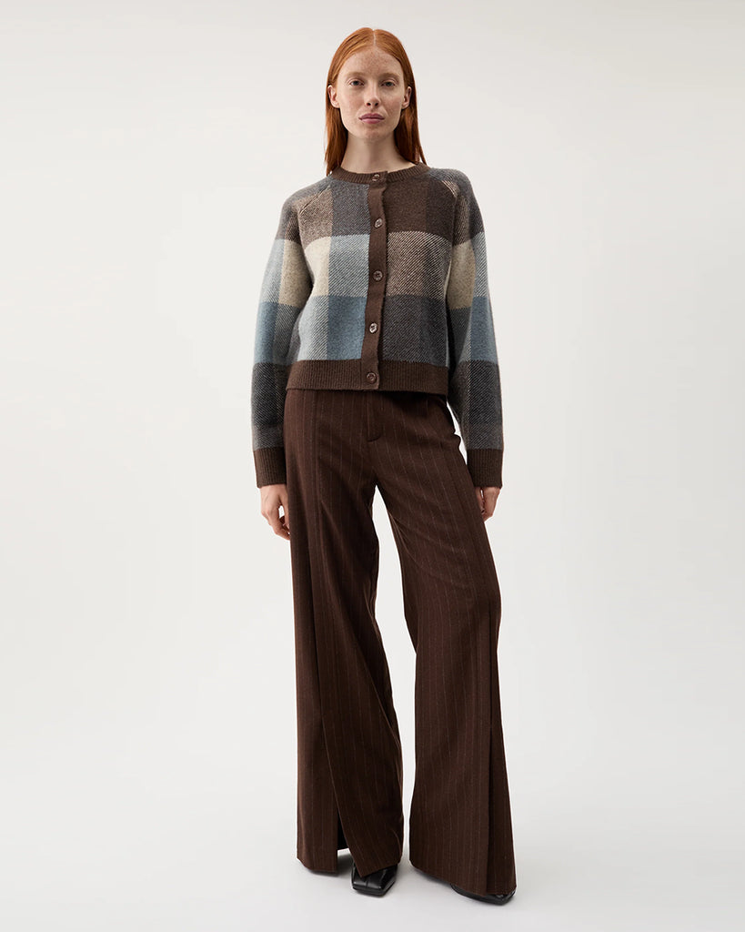 Pudełkowy, ciepły sweter Nina Chicory Coffee w wielokolorową kratę. Ma okrągły dekolt i luźne rękawy. Zapinany na guziki z przodu. Wykończony brązowymi ściągaczami. Wykonany z miękkiej dzianiny z wełną i alpaką. Idealnie nada się do jesiennych stylizacji.&nbsp;