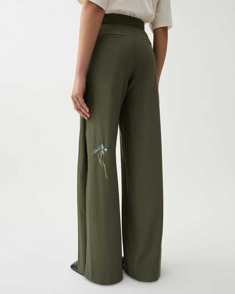 Luźne, garniturowe spodnie Nora Dark Moss w kolorze oliwkowej zieleni z haftowanymi zdobieniami w postaci kwiatów, wysokim stanem i kantem. Posiadają długą, rozszerzaną nogawkę. Mają elastyczny pas w talii i boczne kieszenie. Wykonane z lejącego, dzianinowego materiału zapewniającego komfort i swobodę ruchów. Zestaw je z marynarką Stand Dark Moss tej samej marki.
