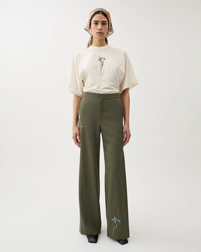 Luźne, garniturowe spodnie Nora Dark Moss w kolorze oliwkowej zieleni z haftowanymi zdobieniami w postaci kwiatów, wysokim stanem i kantem. Posiadają długą, rozszerzaną nogawkę. Mają elastyczny pas w talii i boczne kieszenie. Wykonane z lejącego, dzianinowego materiału zapewniającego komfort i swobodę ruchów. Zestaw je z marynarką Stand Dark Moss tej samej marki.
