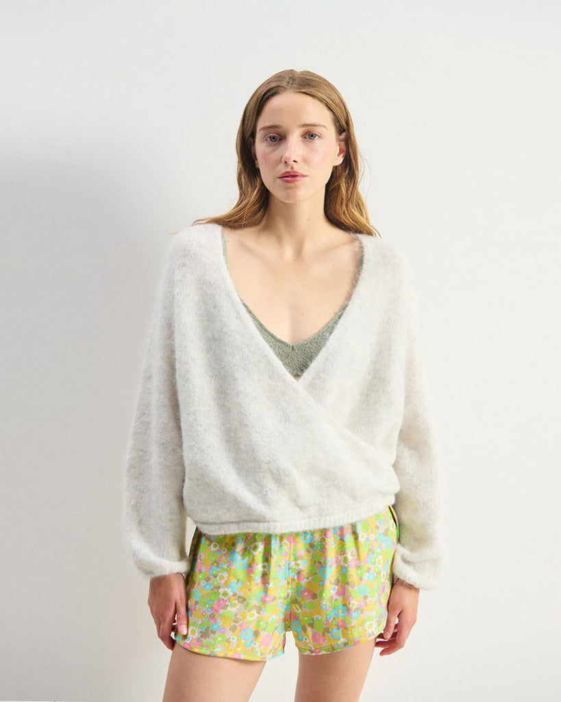 Miękki, krótki sweter NUN18 Polar Melange marki American Vintage z długimi rękawami i głębokim, skrzyżowanym kołnierzem. Wykończony ściągaczami. Wykonany z ciepłej dzianiny z alpaką. Jego kulisty kształt i kopertowy dekolt sprawiają, że jest to kobiecy, a zarazem wygodny element garderoby. Noś go z jeansami, spódnicą lub legginsami.&nbsp;