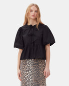 Luźna, czarna bluzka 7364 Cotton Poplin Peplum marki GANNI z&nbsp;okrągłym dekoltem i krótkimi, bufiastymi rękawami o długości do łokcia. Wiązana z przodu za pomocą sznurków. Odcięta wysoko w talii i rozkloszowana u dołu. Wykonana z bawełny organicznej.&nbsp;Idealna do jeansów z wysokim stanem.&nbsp;

-Luźny fason

-100% bawełna organiczna

-Zamów bluzkę w swoim standardowym rozmiarze