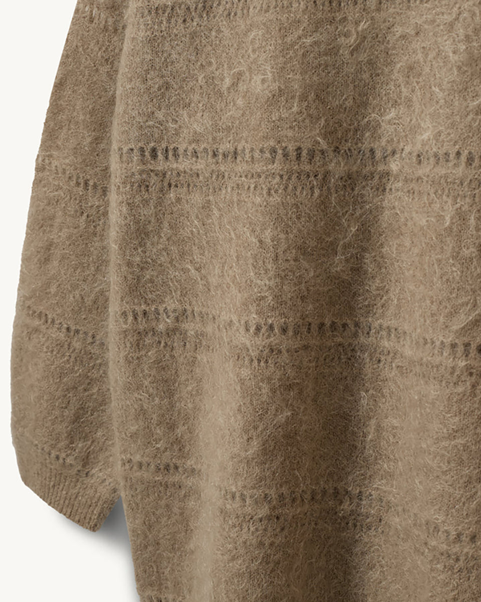 Luźny, oversizowy sweter Roma The Garment w klasycznym odcieniu jasnego brązu. Posiada prosty, okrągły dekolt i lekko opadające ramiona. Sweter ma długie rękawy. Jego powierzchnię wyróżnia urozmaicona faktura- gładką dzianinę przeplatają poziome pasy o dekoracyjnym, ażurowym splocie, które dodają całości lekkości i unikalnego charakteru. Jest wykończony ściągaczami. Wykonany z puchatej dzianiny z moherem.

-Luźny fason

-Okrągły dekolt

-Dzianina z moherem

-Zamów sweter w swoim normalnym rozmiarze