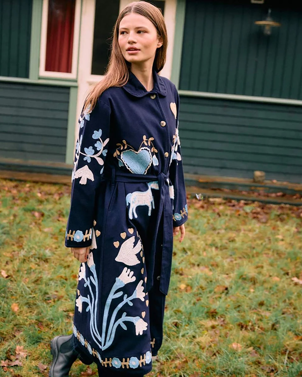 Długi, granatowy płaszcz Rose Navy Horses marki SISSEL EDELBO wykonany z płótna z bawełny organicznej. Posiada podszewkę w bawełniane paski. Model ten wyróżnia się klasycznym kołnierzem, guzikami imitującymi kość oraz paskiem w talii. Ma klasyczne rękawy i jest w całości ozdobiony haftem typu suzani przedstawiającym motywy kwiatów serc i koni. Ma długość do połowy łydki.

-ONE SIZE

-Haft suzani z uroczymi motywami

-100% bawełna organiczna