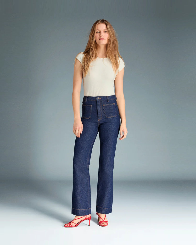 Granatowe jeansy o kobiecym fasonie Belleville Rouje z wysokim stanem i lekko rozszerzaną u dołu nogawką. Dopasowane w biodrach i udach. Z przodu posiadają naszyte, prostokątne kieszenie. Zapinane na zamek błyskawiczny i guzik. Obszyte kontrastową, rudą nicią