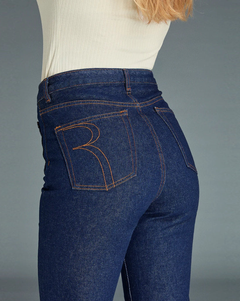 Granatowe jeansy o kobiecym fasonie Belleville Rouje z wysokim stanem i lekko rozszerzaną u dołu nogawką. Dopasowane w biodrach i udach. Z przodu posiadają naszyte, prostokątne kieszenie. Zapinane na zamek błyskawiczny i guzik. Obszyte kontrastową, rudą nicią