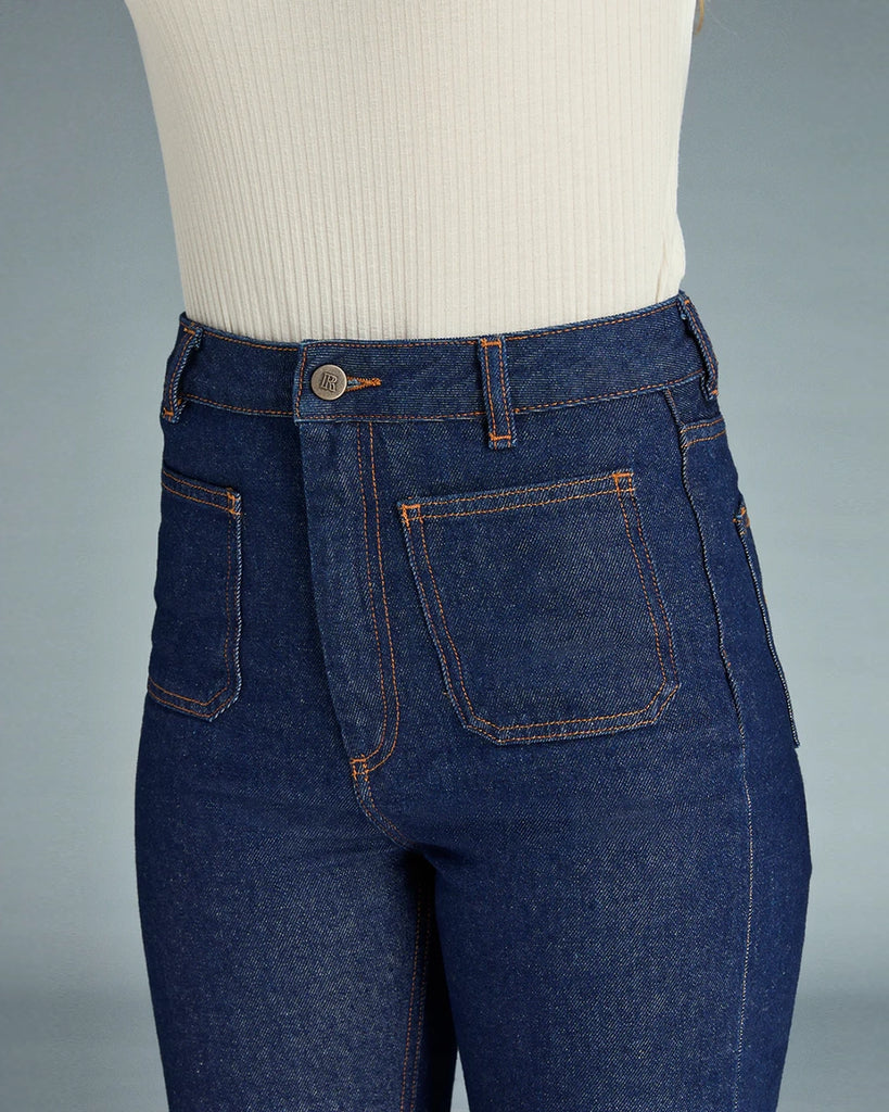 Granatowe jeansy o kobiecym fasonie Belleville Rouje z wysokim stanem i lekko rozszerzaną u dołu nogawką. Dopasowane w biodrach i udach. Z przodu posiadają naszyte, prostokątne kieszenie. Zapinane na zamek błyskawiczny i guzik. Obszyte kontrastową, rudą nicią
