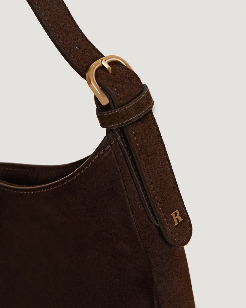 Zamszowa, brązowa torebka o średniej wielkości Big Rouje z zaokrąglonymi kątami i krótkim, regulowanym paskiem do wygodnego trzymania w dłoni i zawieszenia na ramieniu. Zapinana za pomocą magnesu. Wewnątrz obszyta różową, satynową podszewką.