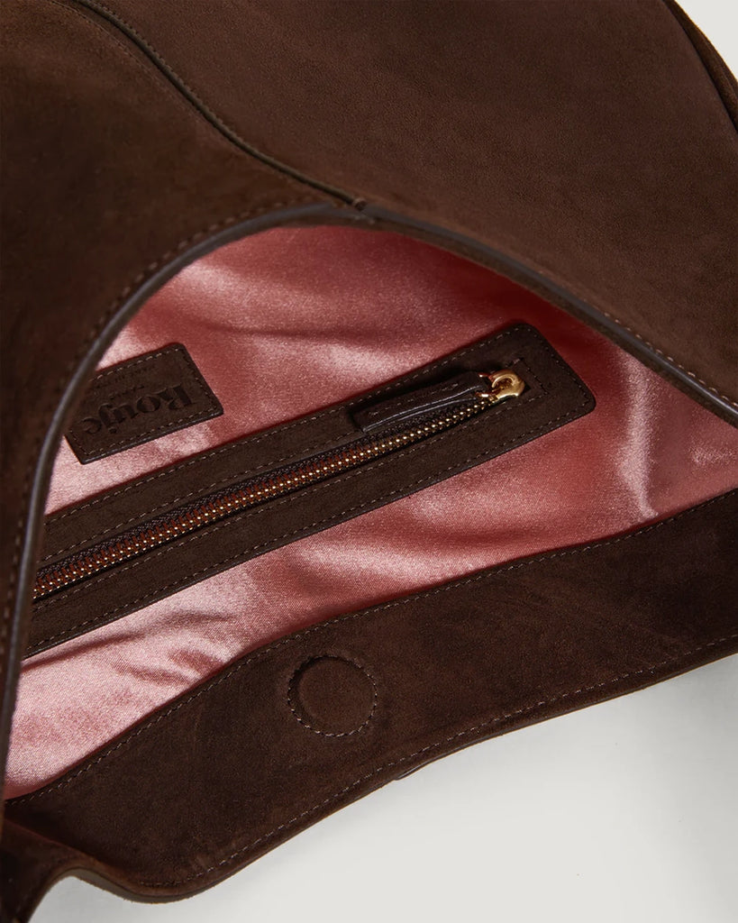 Zamszowa, brązowa torebka o średniej wielkości Big Rouje z zaokrąglonymi kątami i krótkim, regulowanym paskiem do wygodnego trzymania w dłoni i zawieszenia na ramieniu. Zapinana za pomocą magnesu. Wewnątrz obszyta różową, satynową podszewką.