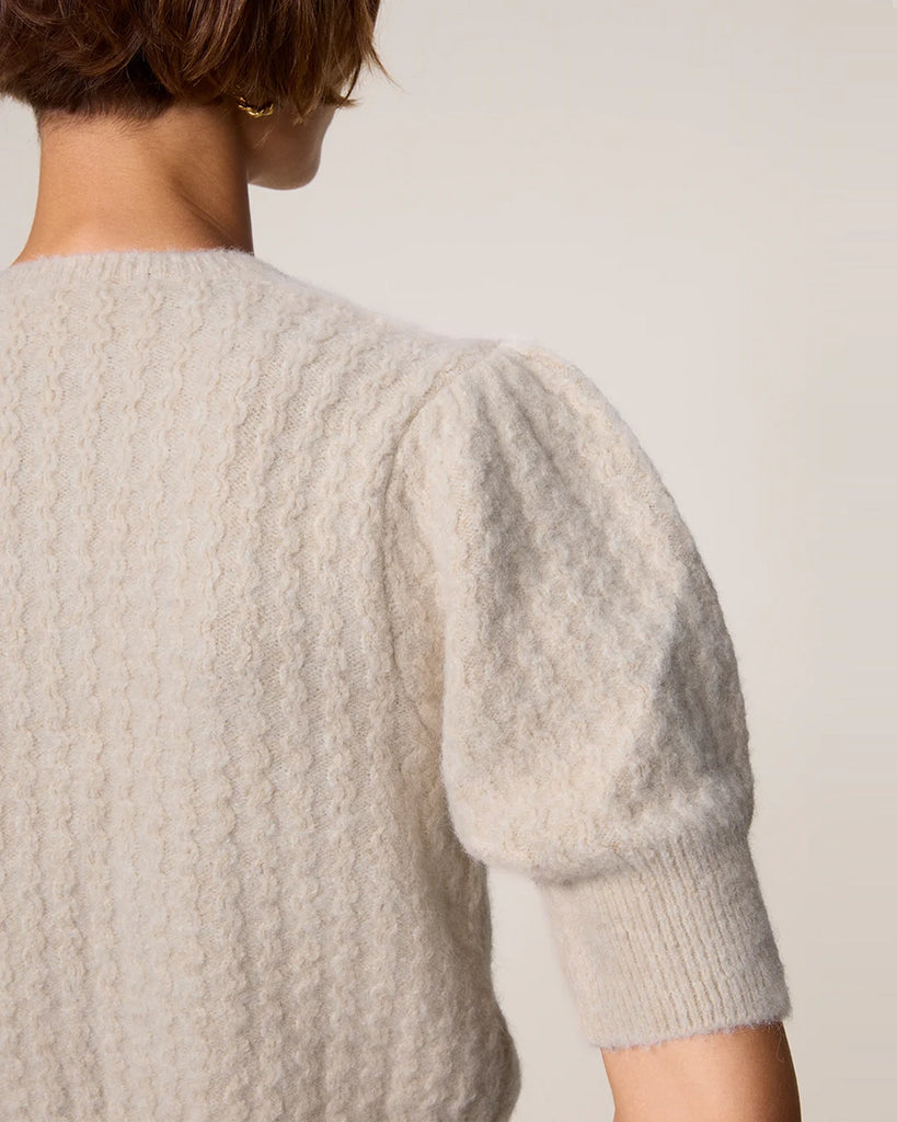 Krótki kardigan z bufiastymi rękawami przed łokieć Cassia Rouje. Posiada okrągły dekolt. Zapinany na drobne guziki z masy perłowej. Sweter ma prosty krój i jest wykończony ściągaczami.