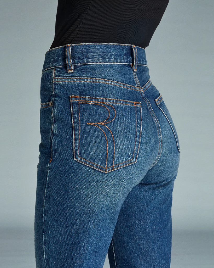 Granatowe jeansy o kobiecym fasonie Concorde Rouje z wysokim stanem i rozszerzaną u dołu, skróconą nogawką. Dopasowane w biodrach i udach. Posiadają pięć kieszeni. Nad lewą kieszenią znajduje się niewielka, haftowana litera R. Zapinane na zamek błyskawiczny i guzik. To model pięknie podkreślający sylwetkę. 