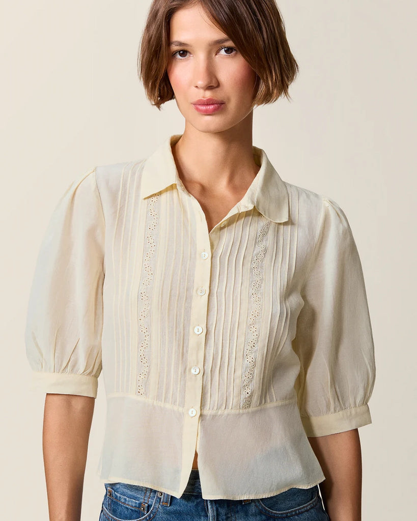 Luźna, kremowa bluzka Dorothea Rouje z krótkim, bufiastym rękawem i kołnierzykiem. Plisowana i haftowana na dekolcie. Zapinana na guziki z masy perłowej. Lekko wcięta w talii. Wykonana z cienkiej i zwiewnej tkaniny z bawełny i wiskozy