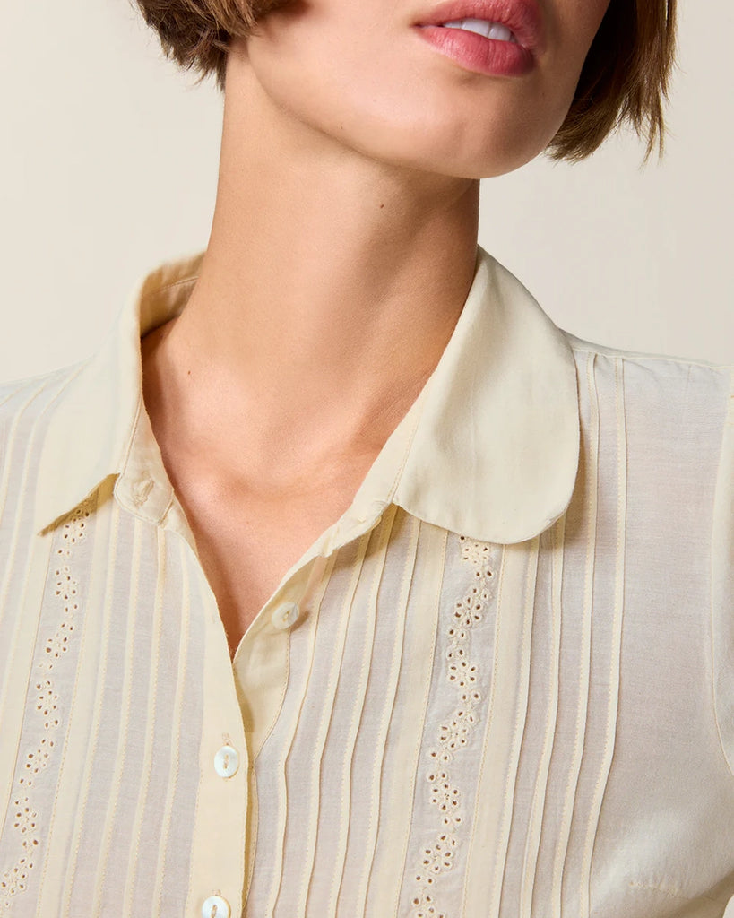 Luźna, kremowa bluzka Dorothea Rouje z krótkim, bufiastym rękawem i kołnierzykiem. Plisowana i haftowana na dekolcie. Zapinana na guziki z masy perłowej. Lekko wcięta w talii. Wykonana z cienkiej i zwiewnej tkaniny z bawełny i wiskozy