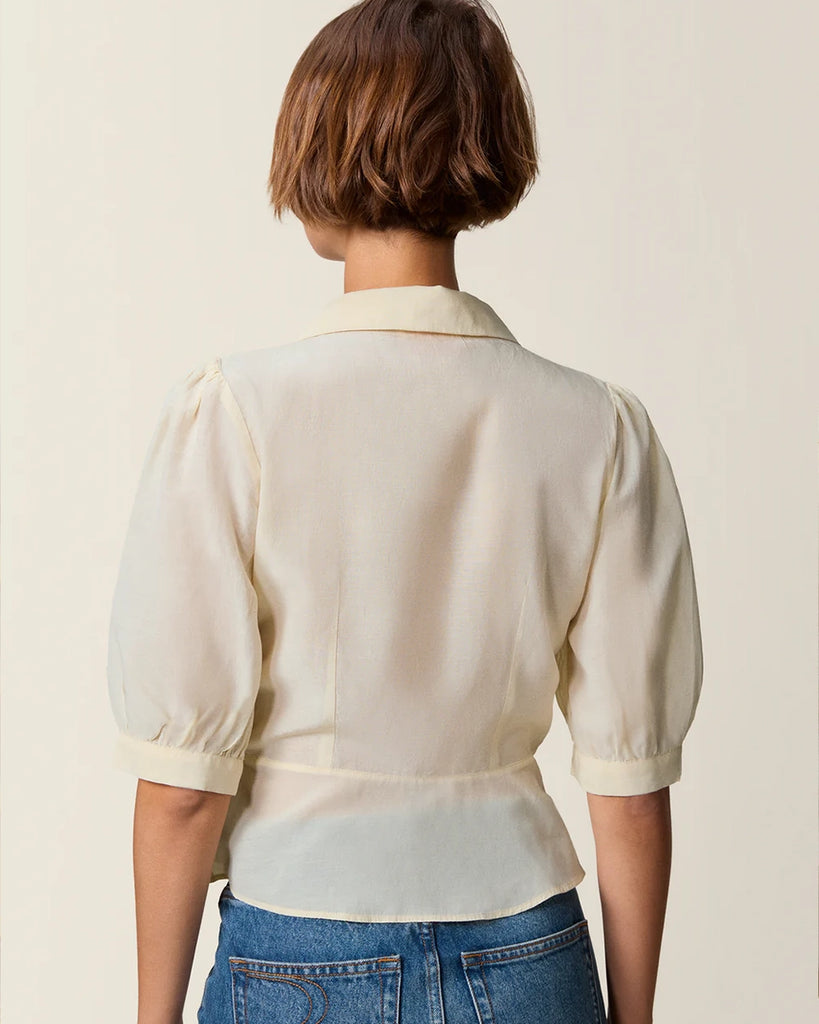 Luźna, kremowa bluzka Dorothea Rouje z krótkim, bufiastym rękawem i kołnierzykiem. Plisowana i haftowana na dekolcie. Zapinana na guziki z masy perłowej. Lekko wcięta w talii. Wykonana z cienkiej i zwiewnej tkaniny z bawełny i wiskozy