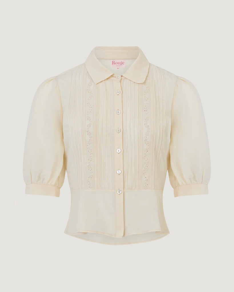Luźna, kremowa bluzka Dorothea Rouje z krótkim, bufiastym rękawem i kołnierzykiem. Plisowana i haftowana na dekolcie. Zapinana na guziki z masy perłowej. Lekko wcięta w talii. Wykonana z cienkiej i zwiewnej tkaniny z bawełny i wiskozy