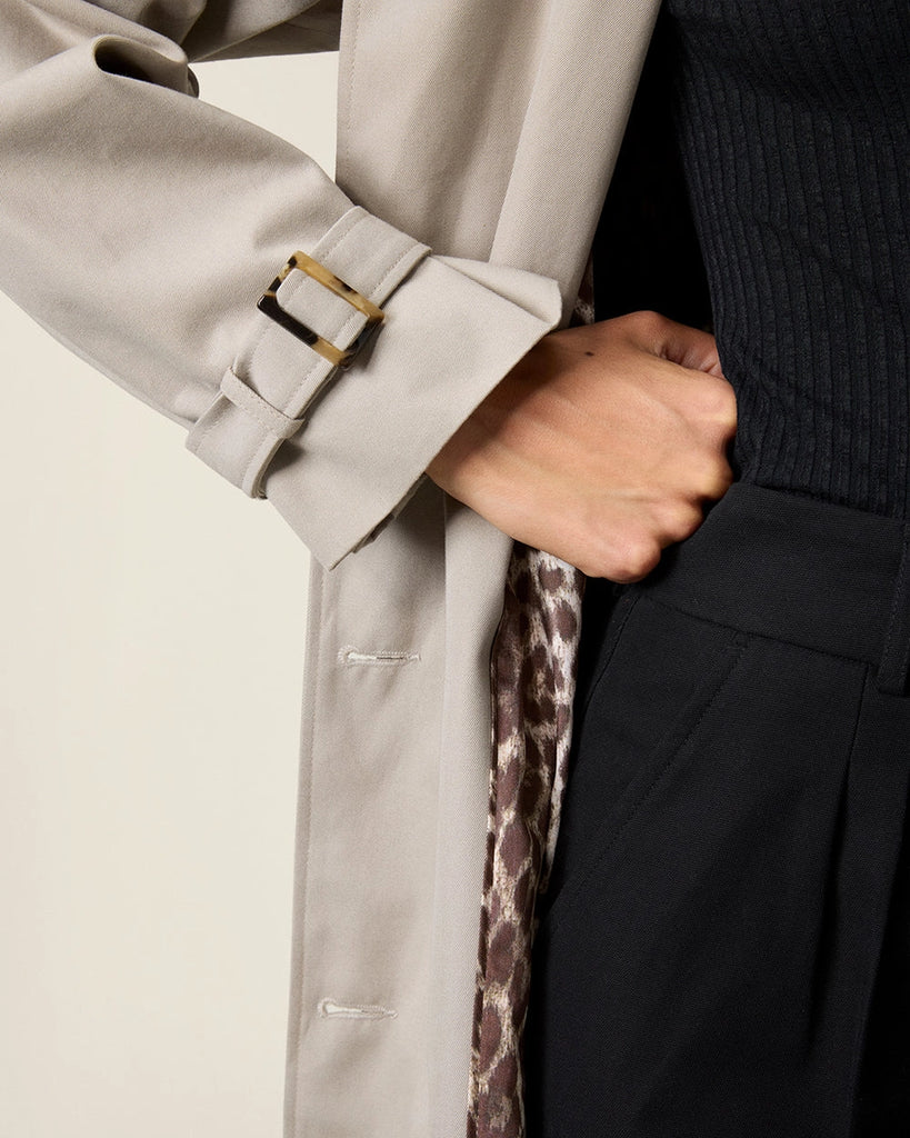 Klasyczny luźny, dwurzędowy prochowiec Ezra Rouje wiązany w talii za pomocą wyciąganego, szerokiego paska. Posiada kołnierzyk, pagony na ramionach i luźne rękawy z paskami przy mankietach. Z tyłu u dołu ma rozcięcie. Płaszcz posiada dwie, boczne kieszenie i podszewkę we wzór w panterę. Jest zapinany na guziki imitujące poroże.