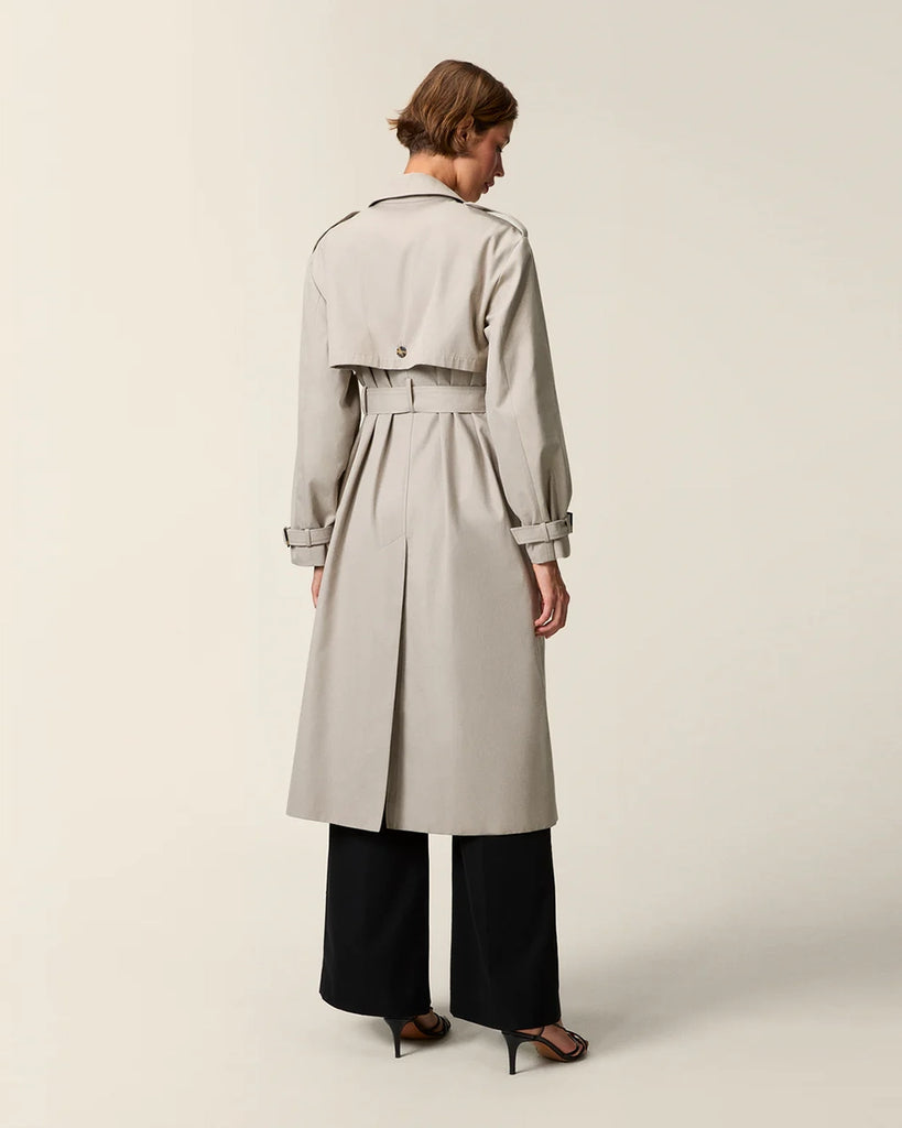 Klasyczny luźny, dwurzędowy prochowiec Ezra Rouje wiązany w talii za pomocą wyciąganego, szerokiego paska. Posiada kołnierzyk, pagony na ramionach i luźne rękawy z paskami przy mankietach. Z tyłu u dołu ma rozcięcie. Płaszcz posiada dwie, boczne kieszenie i podszewkę we wzór w panterę. Jest zapinany na guziki imitujące poroże.