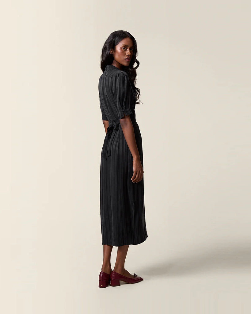 Czarna sukienka midi w paski Laureline Rouje z krótkimi, bufiastymi rękawami, trójkątnym dekoltem i kołnierzykiem. Zapinana na guziki. Dopasowana i wiązana z tyłu w talii za pomocą paska. Sukienka ma długość do połowy łydki.