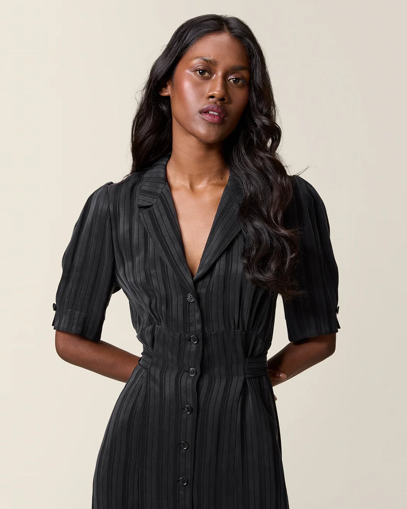 Czarna sukienka midi w paski Laureline Rouje z krótkimi, bufiastymi rękawami, trójkątnym dekoltem i kołnierzykiem. Zapinana na guziki. Dopasowana i wiązana z tyłu w talii za pomocą paska. Sukienka ma długość do połowy łydki.