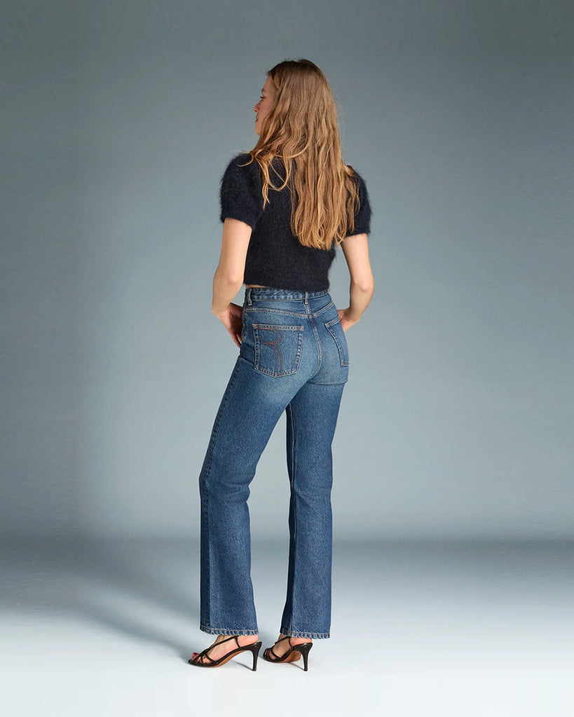 Granatowe jeansy o kobiecym fasonie Madeleine Rouje z wysokim stanem i rozszerzaną u dołu nogawką. Dopasowane w biodrach i udach. Posiadają pięć kieszeni. Nad lewą kieszenią znajduje się niewielka, haftowana litera R. Zapinane na zamek błyskawiczny i guzik.