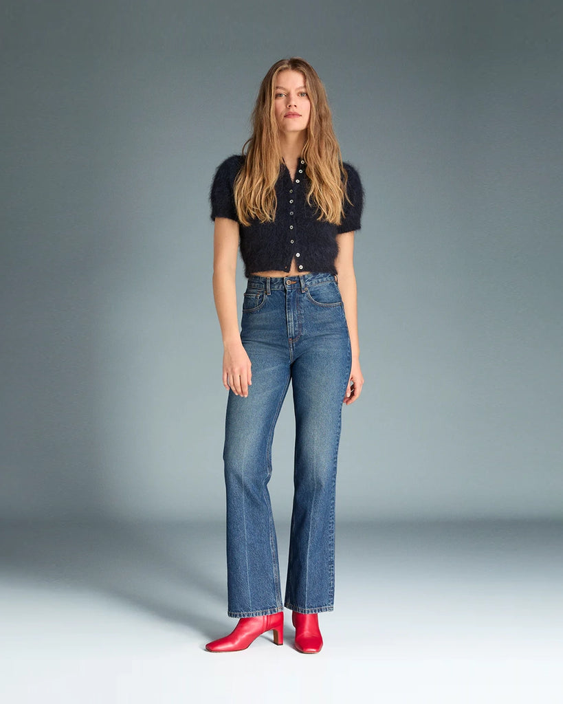 Granatowe jeansy o kobiecym fasonie Madeleine Rouje z wysokim stanem i rozszerzaną u dołu nogawką. Dopasowane w biodrach i udach. Posiadają pięć kieszeni. Nad lewą kieszenią znajduje się niewielka, haftowana litera R. Zapinane na zamek błyskawiczny i guzik.