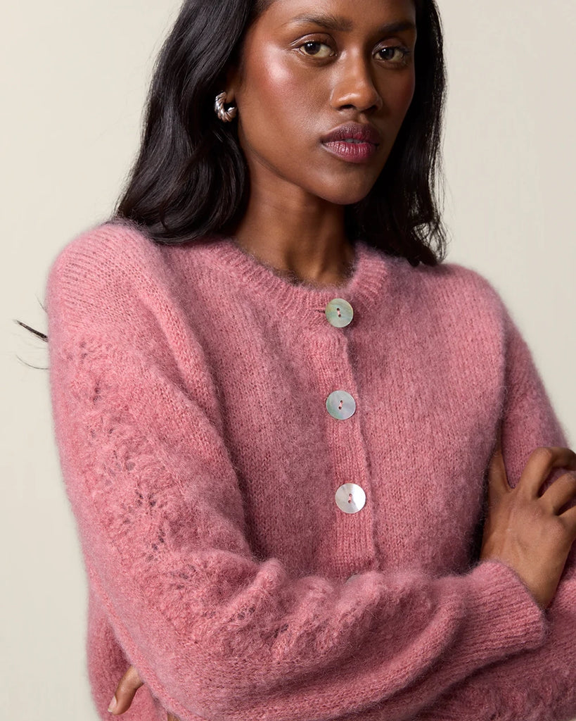 Luźny, moherowy kardigan Maina Rouje z okrągłym dekoltem i balonowymi, reglanowymi rękawami z ażurowym wzorem na bokach. Zapinany na duże guziki z masy perłowej. Posiada prosty krój. Jest wykończony ściągaczami