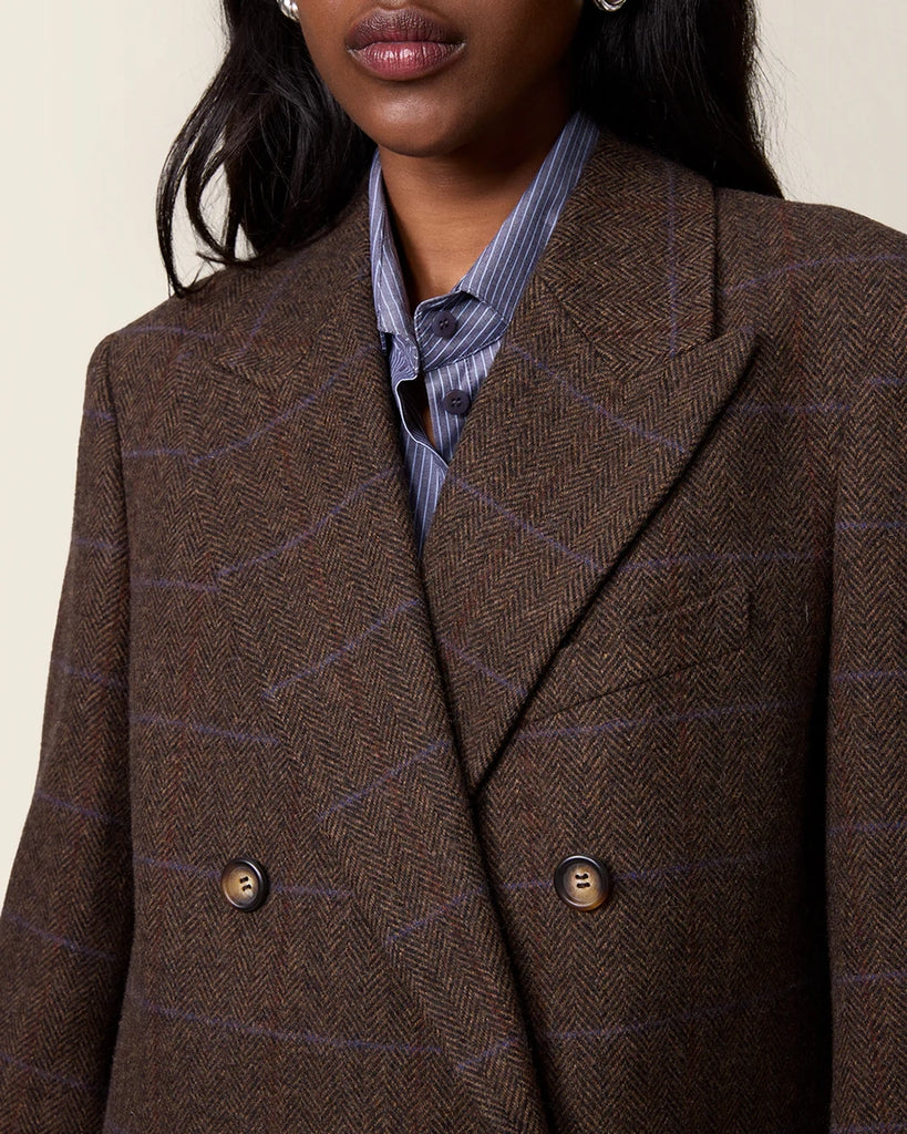 Klasyczna, dwurzędowa marynarka w kratkę z wełną Marcel Rouje. Posiada prosty krój, dekolt w kształcie litery V i klapy. Marynarka ma dwie, przednie kieszenie i rozcięcie z tyłu oraz podszewkę. Zapinana na guziki imitujące poroże.