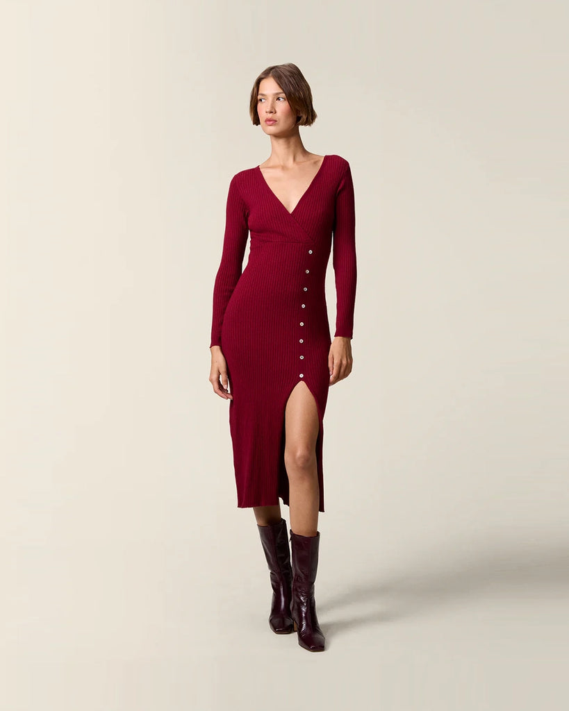 Dzianinowa sukienka midi Mila Rouje z głębokim, trójkątnym dekoltem i długimi, wąskimi rękawami. Z boku posiada guziki z masy perłowej. U dołu ma głębokie rozcięcie. Sukienka posiada przylegający fason, który pięknie eksponuje sylwetkę oraz długość do połowy łydki