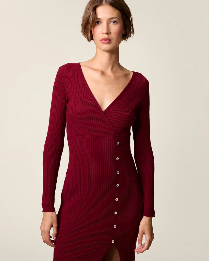 Dzianinowa sukienka midi Mila Rouje z głębokim, trójkątnym dekoltem i długimi, wąskimi rękawami. Z boku posiada guziki z masy perłowej. U dołu ma głębokie rozcięcie. Sukienka posiada przylegający fason, który pięknie eksponuje sylwetkę oraz długość do połowy łydki