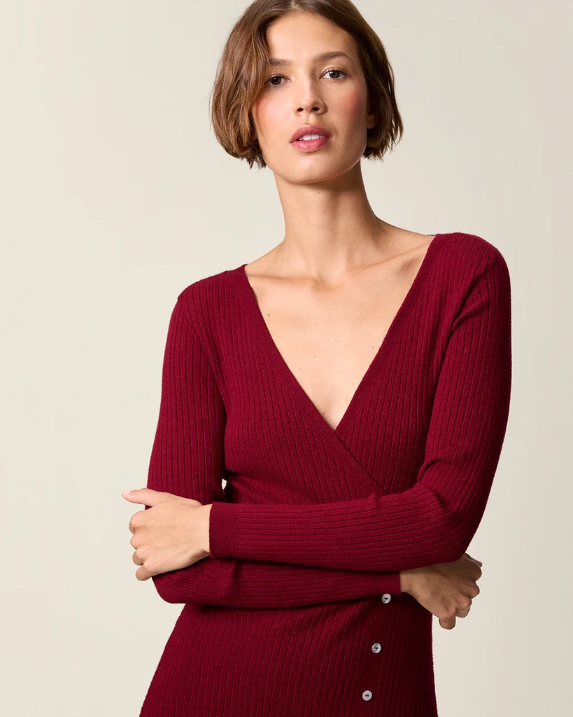 Dzianinowa sukienka midi Mila Rouje z głębokim, trójkątnym dekoltem i długimi, wąskimi rękawami. Z boku posiada guziki z masy perłowej. U dołu ma głębokie rozcięcie. Sukienka posiada przylegający fason, który pięknie eksponuje sylwetkę oraz długość do połowy łydki