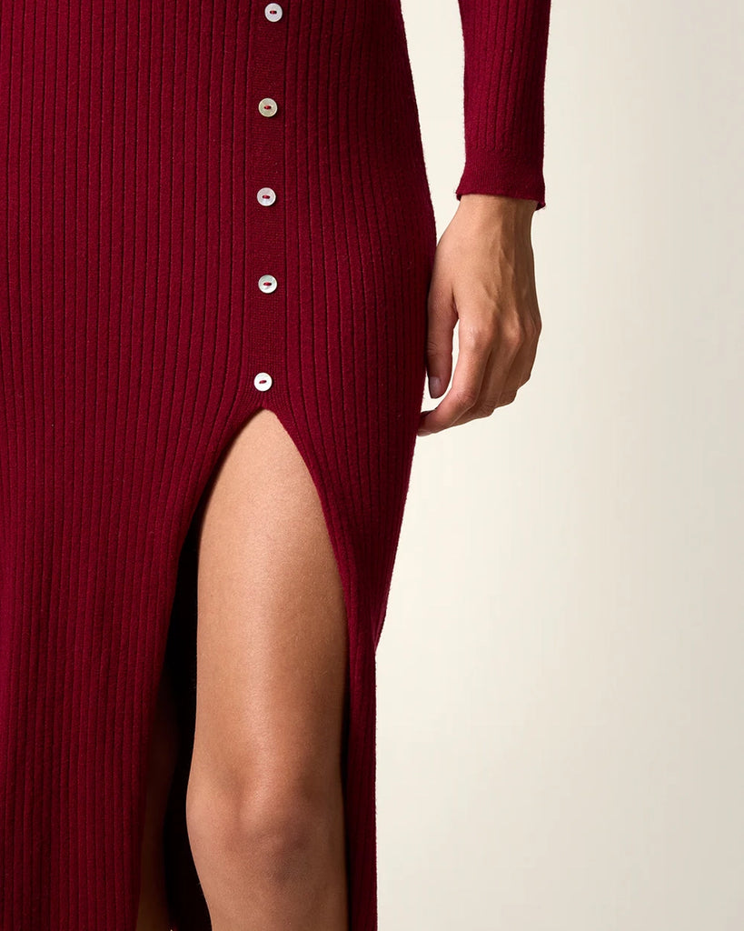 Dzianinowa sukienka midi Mila Rouje z głębokim, trójkątnym dekoltem i długimi, wąskimi rękawami. Z boku posiada guziki z masy perłowej. U dołu ma głębokie rozcięcie. Sukienka posiada przylegający fason, który pięknie eksponuje sylwetkę oraz długość do połowy łydki