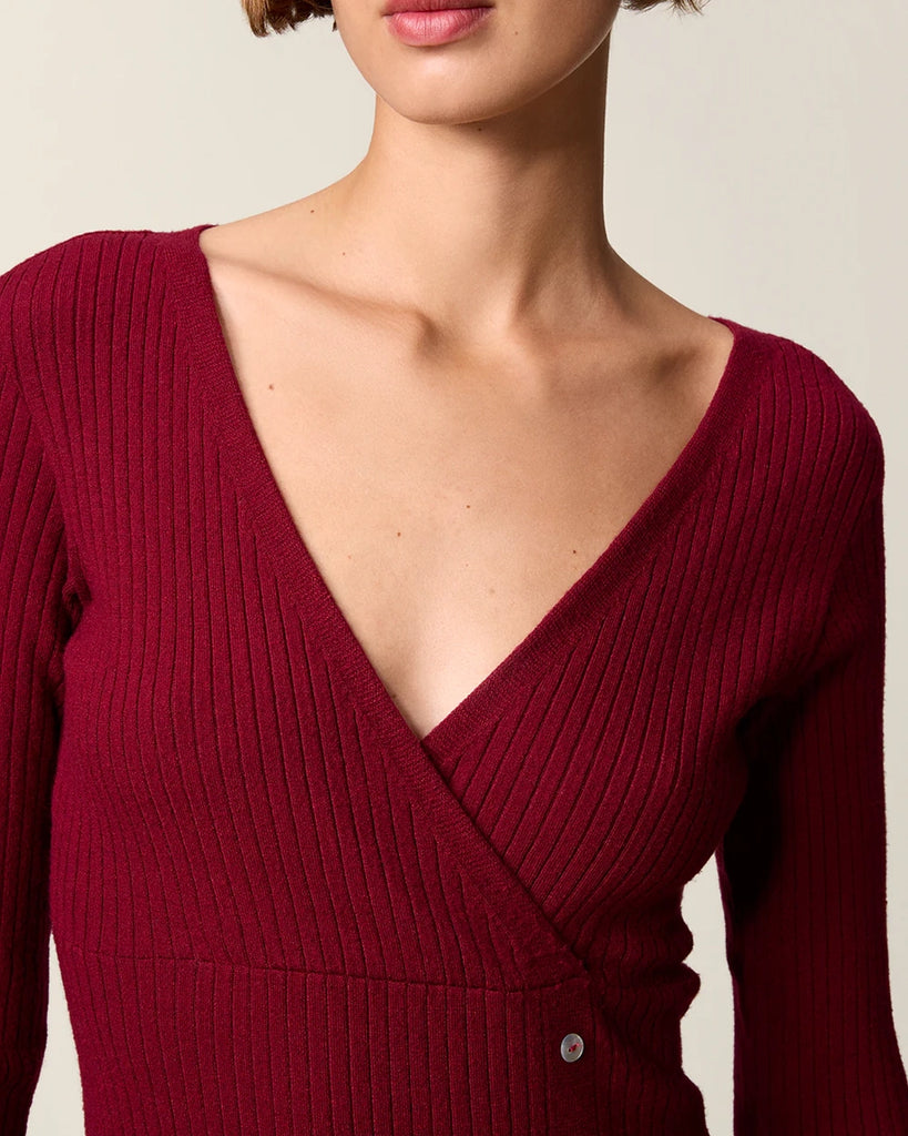 Dzianinowa sukienka midi Mila Rouje z głębokim, trójkątnym dekoltem i długimi, wąskimi rękawami. Z boku posiada guziki z masy perłowej. U dołu ma głębokie rozcięcie. Sukienka posiada przylegający fason, który pięknie eksponuje sylwetkę oraz długość do połowy łydki