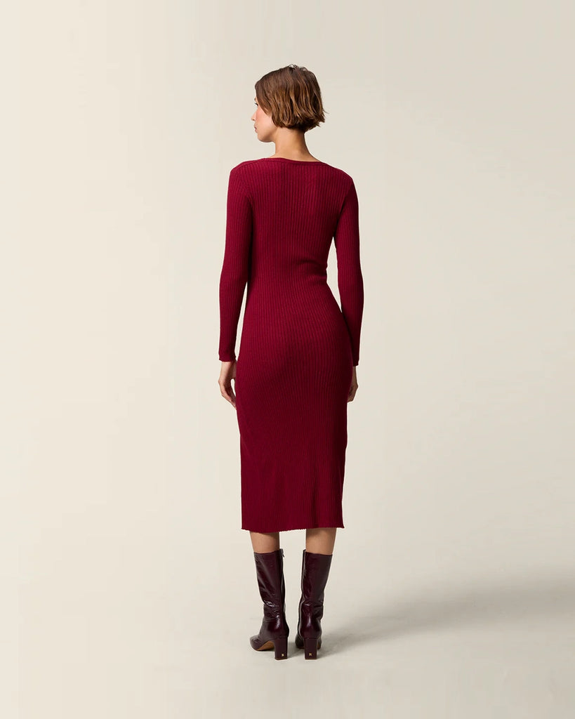 Dzianinowa sukienka midi Mila Rouje z głębokim, trójkątnym dekoltem i długimi, wąskimi rękawami. Z boku posiada guziki z masy perłowej. U dołu ma głębokie rozcięcie. Sukienka posiada przylegający fason, który pięknie eksponuje sylwetkę oraz długość do połowy łydki