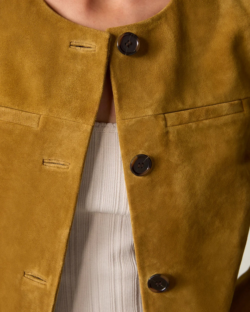 Krótka, zamszowa kurtka o pudełkowym fasonie Milo Rouje z okrągłym dekoltem. Zapinana na duże, szylkretowe guziki. Posiada dwie kieszenie nad piersiami.